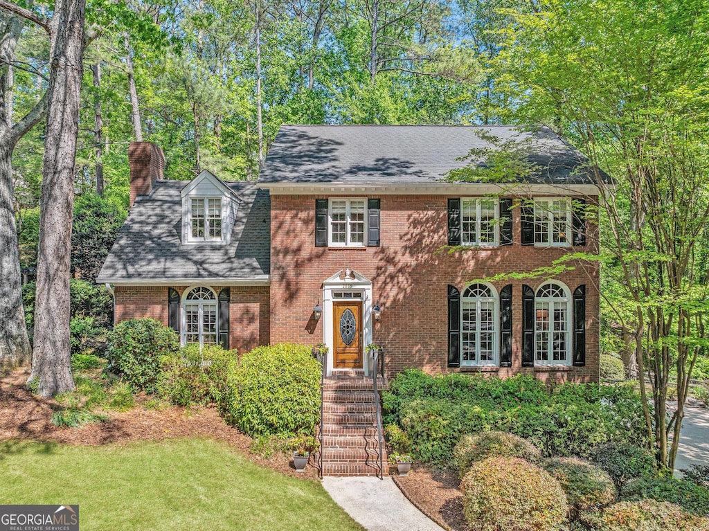 view of front of home featuring brick siding, a shingled roof, a chimney, and a front lawn