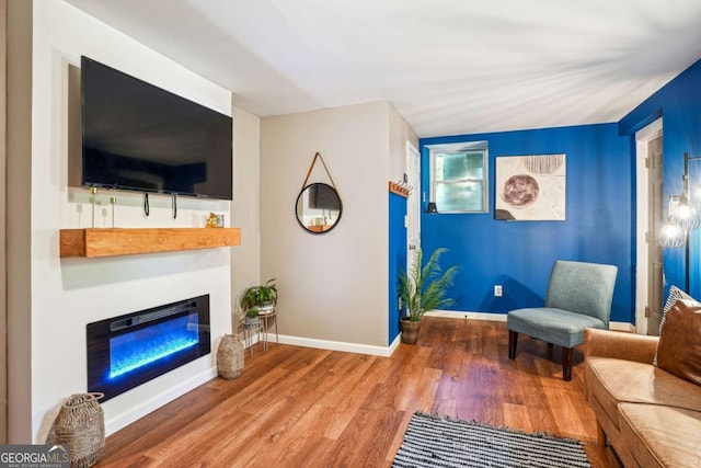 sitting room with baseboards, a glass covered fireplace, and wood finished floors