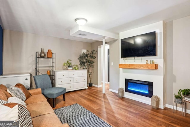 living room featuring baseboards, a glass covered fireplace, wood finished floors, and visible vents