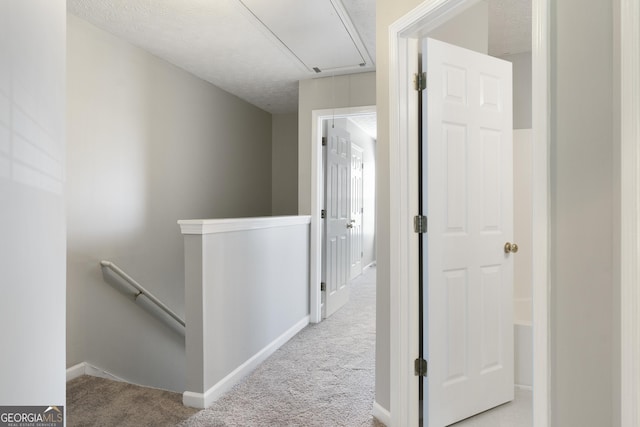 hall featuring attic access, baseboards, carpet floors, and an upstairs landing