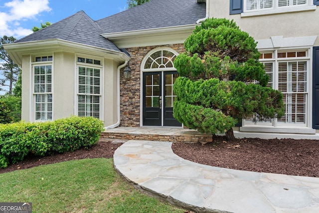 entrance to property featuring stucco siding, roof with shingles, and stone siding