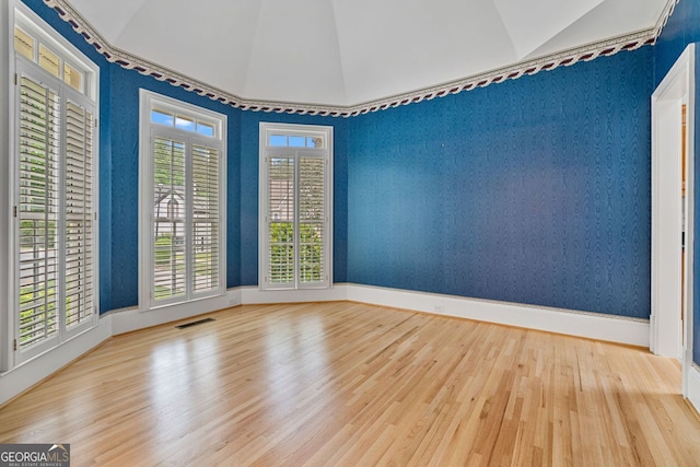 empty room with wood finished floors, lofted ceiling, baseboards, and wallpapered walls