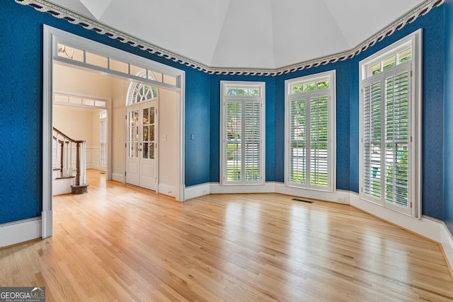unfurnished room with wood finished floors, lofted ceiling, stairs, plenty of natural light, and baseboards