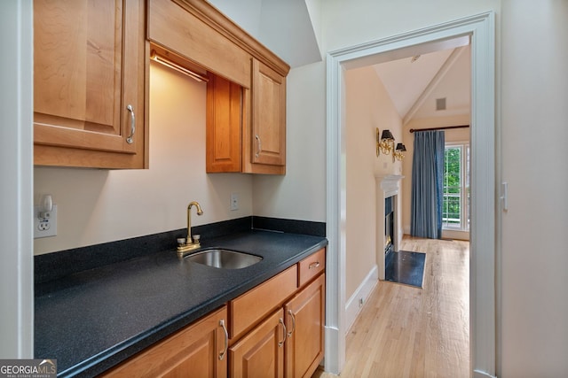 kitchen featuring a sink, dark countertops, light wood-style flooring, vaulted ceiling, and a fireplace with flush hearth