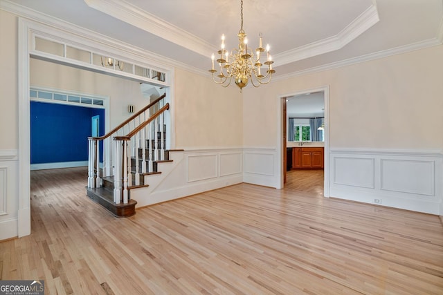 unfurnished dining area featuring light wood-style flooring, a chandelier, stairway, ornamental molding, and a raised ceiling