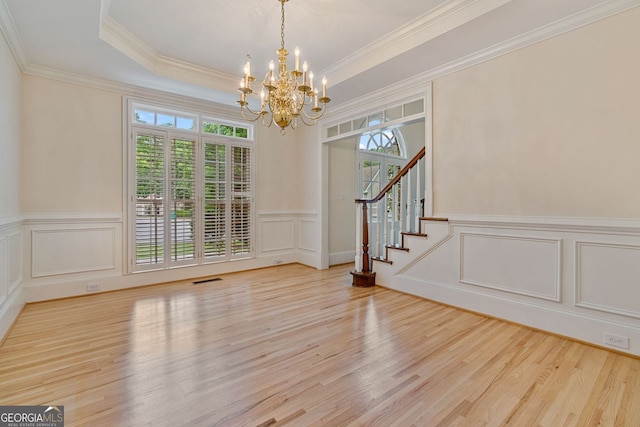 unfurnished dining area with a decorative wall, a chandelier, wood finished floors, stairway, and wainscoting