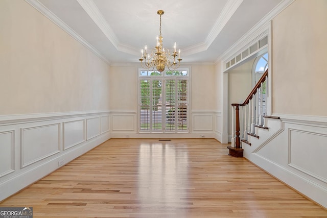 unfurnished dining area with a chandelier, light wood-style floors, a decorative wall, stairway, and wainscoting