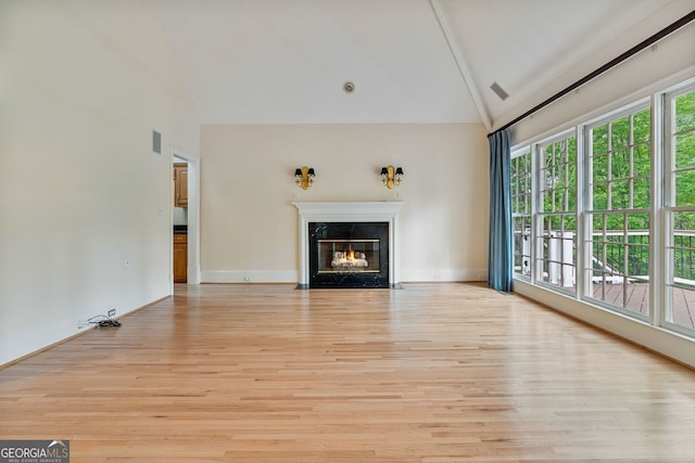 unfurnished living room featuring high vaulted ceiling, light wood-type flooring, a premium fireplace, and baseboards