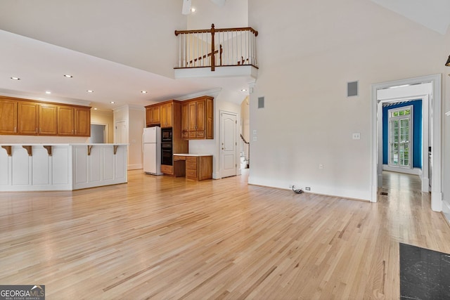 unfurnished living room with light wood-type flooring, a towering ceiling, recessed lighting, and baseboards