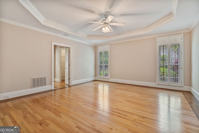 empty room with a tray ceiling, healthy amount of natural light, hardwood / wood-style floors, ornamental molding, and ceiling fan