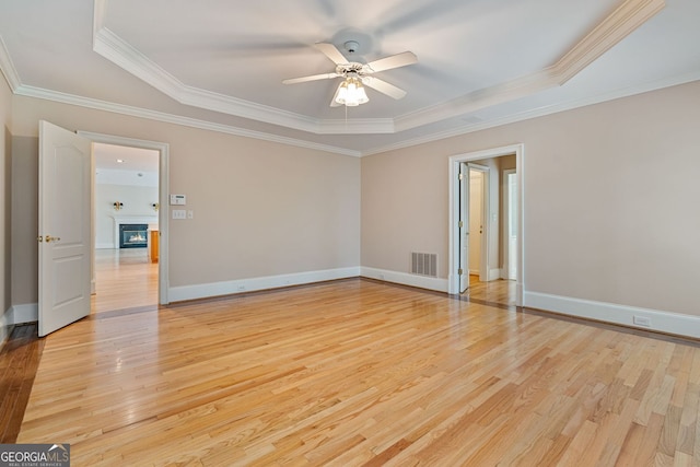 unfurnished room with a tray ceiling, ceiling fan, light wood-style floors, ornamental molding, and baseboards