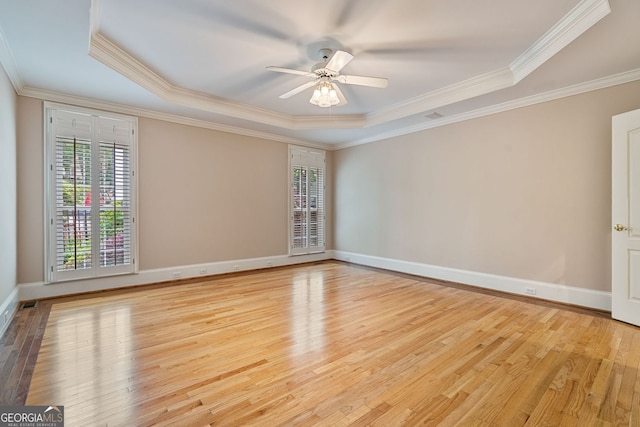 spare room with a tray ceiling, ornamental molding, wood finished floors, a ceiling fan, and baseboards
