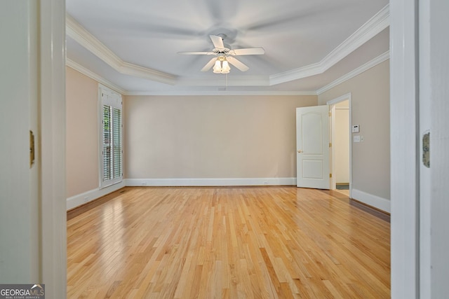 empty room with light wood finished floors, ceiling fan, ornamental molding, a tray ceiling, and baseboards