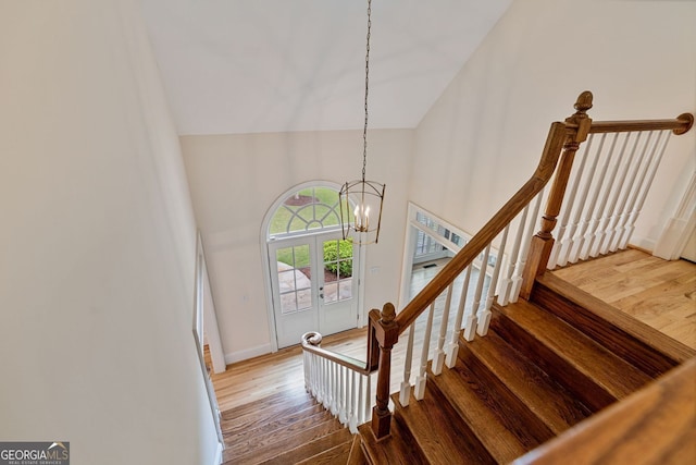 stairway featuring a chandelier, wood-type flooring, a high ceiling, and baseboards