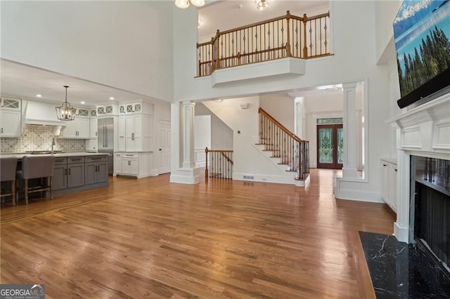 3115 Corsair Curv, Cumming, GA 30040 - unfurnished living room featuring ornate columns, a towering ceiling, a high end fireplace, stairs, and wood finished floors