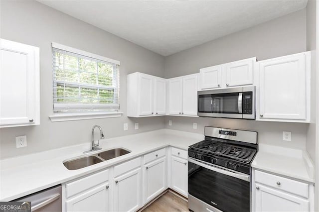 kitchen with white cabinets, appliances with stainless steel finishes, a sink, and light countertops