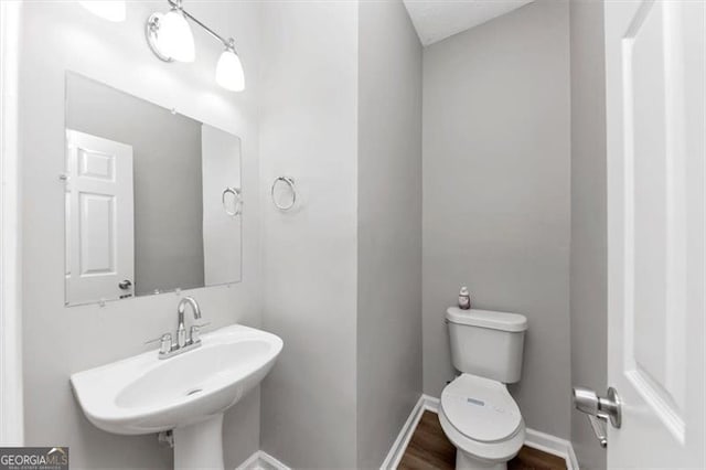 half bathroom featuring wood finished floors, baseboards, a sink, and toilet