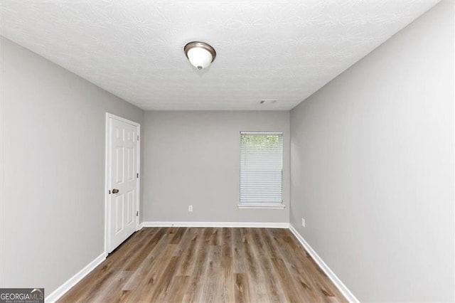 spare room with baseboards, wood finished floors, visible vents, and a textured ceiling