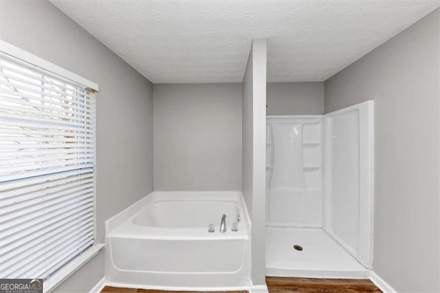 bathroom featuring a bath, wood finished floors, a shower, and a textured ceiling