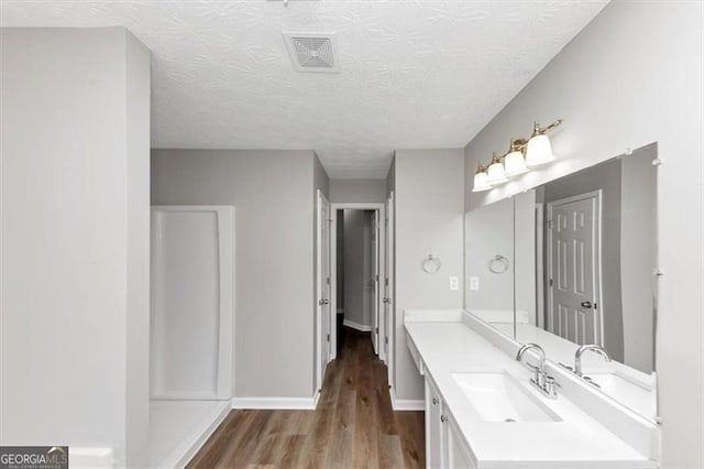 bathroom featuring wood finished floors, a textured ceiling, vanity, baseboards, and visible vents