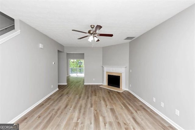 unfurnished living room featuring a fireplace with raised hearth, visible vents, a ceiling fan, light wood-type flooring, and baseboards