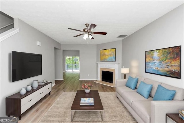 living room featuring light wood-type flooring, baseboards, visible vents, a fireplace with raised hearth, and ceiling fan