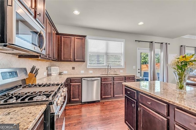 kitchen with a sink, dark wood finished floors, decorative backsplash, light stone countertops, and appliances with stainless steel finishes