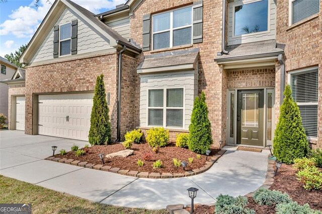view of exterior entry featuring brick siding, an attached garage, and driveway
