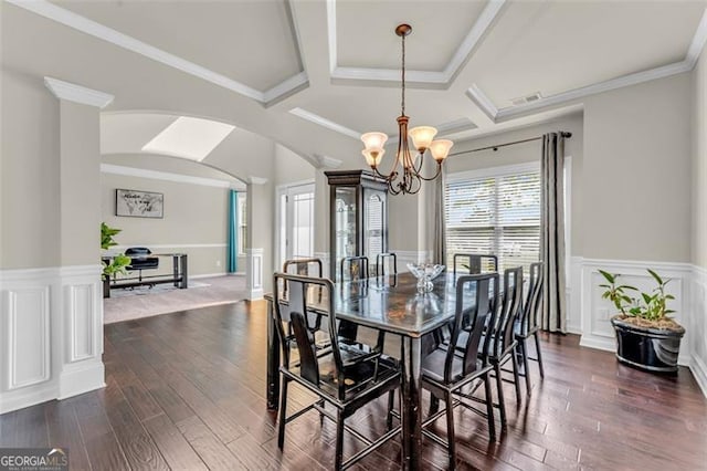 dining room with dark wood finished floors, a wainscoted wall, coffered ceiling, arched walkways, and a notable chandelier