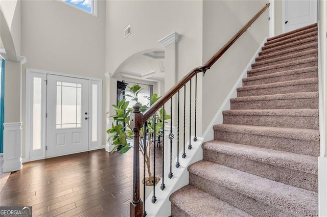 foyer entrance featuring dark wood-style flooring, decorative columns, visible vents, a high ceiling, and stairway