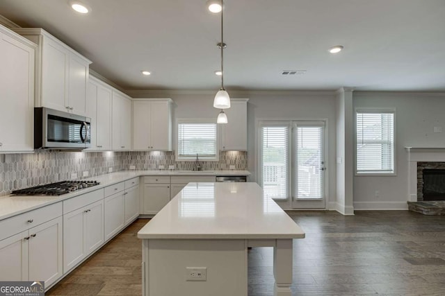 7208 Whitewater Dr, Flowery Branch, GA 30542 - kitchen with stainless steel appliances, a stone fireplace, decorative backsplash, a kitchen island, and ornamental molding