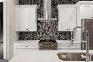 kitchen featuring decorative backsplash, light countertops, white cabinetry, wall chimney exhaust hood, and a sink