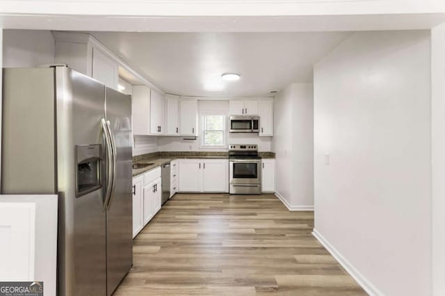 3556 Finch Rd SW, Powder Springs, GA 30127 - kitchen with appliances with stainless steel finishes, dark countertops, white cabinetry, light wood-style floors, and baseboards