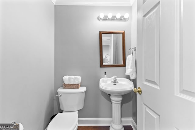 half bathroom featuring wood finished floors, crown molding, baseboards, and toilet