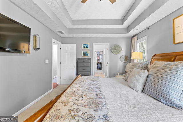 bedroom with a spacious closet, a raised ceiling, visible vents, baseboards, and ceiling fan