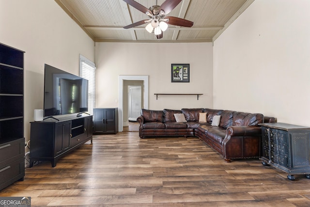 living room featuring ceiling fan, a towering ceiling, wood finished floors, and beamed ceiling