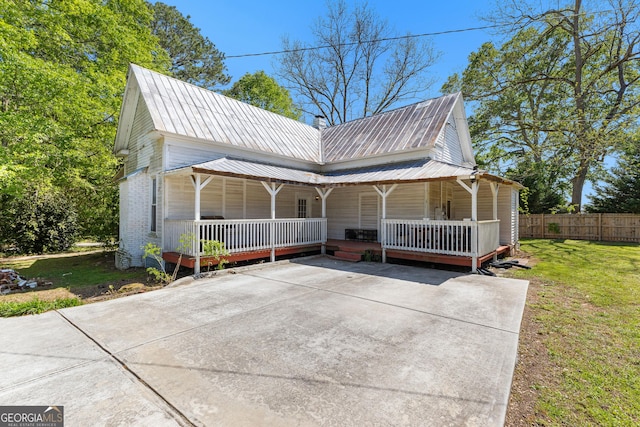 view of front of property with a porch, concrete driveway, metal roof, fence, and a front yard