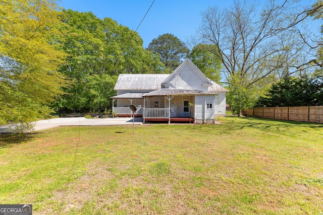rear view of property with a lawn, fence, driveway, and metal roof