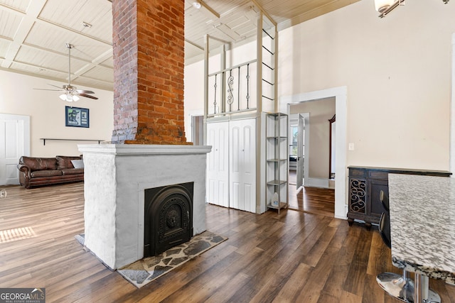 unfurnished living room with a towering ceiling, a ceiling fan, a large fireplace, wood ceiling, and dark wood-type flooring