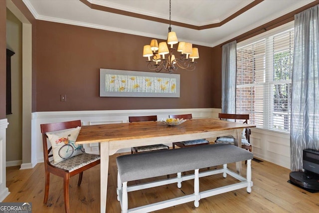 dining room with crown molding, an inviting chandelier, light wood-style flooring, and a raised ceiling