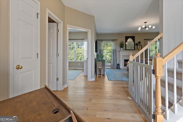 entryway with stairs, baseboards, a lit fireplace, a chandelier, and light wood-style flooring