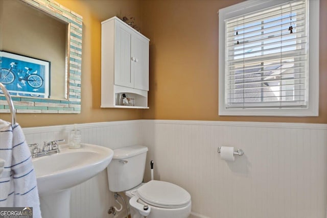 half bath featuring a sink, a wainscoted wall, and toilet