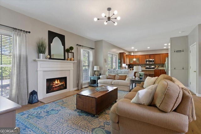 living area featuring recessed lighting, a notable chandelier, a glass covered fireplace, and light wood-type flooring