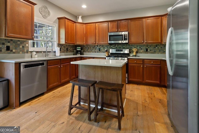 kitchen with light wood-style floors, a center island, light countertops, a sink, and appliances with stainless steel finishes