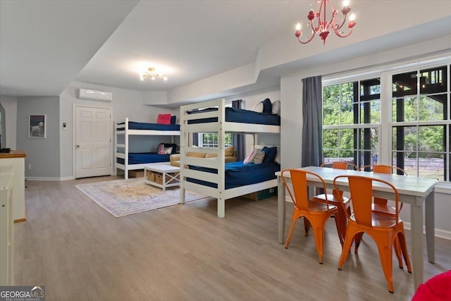bedroom with light wood-style floors, baseboards, an AC wall unit, and a chandelier