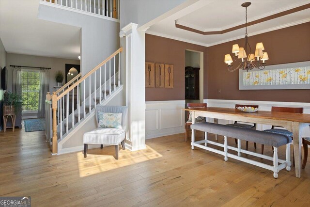 dining area with an inviting chandelier, a raised ceiling, stairs, ornamental molding, and hardwood / wood-style flooring