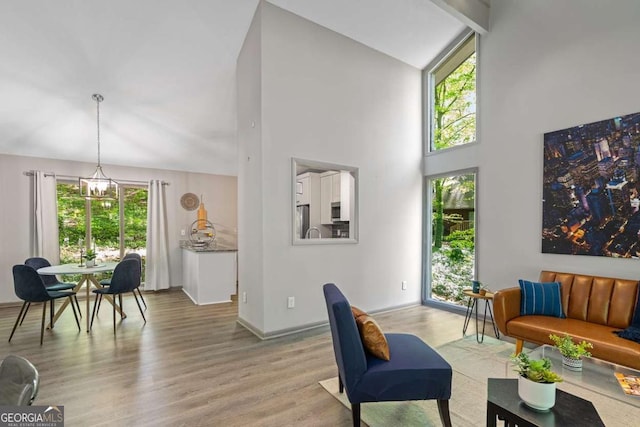 living room featuring light wood-style floors, baseboards, high vaulted ceiling, and a notable chandelier