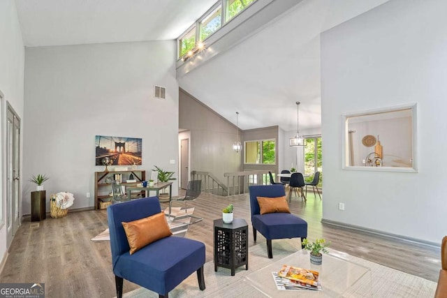 living area featuring high vaulted ceiling, an upstairs landing, wood finished floors, baseboards, and visible vents