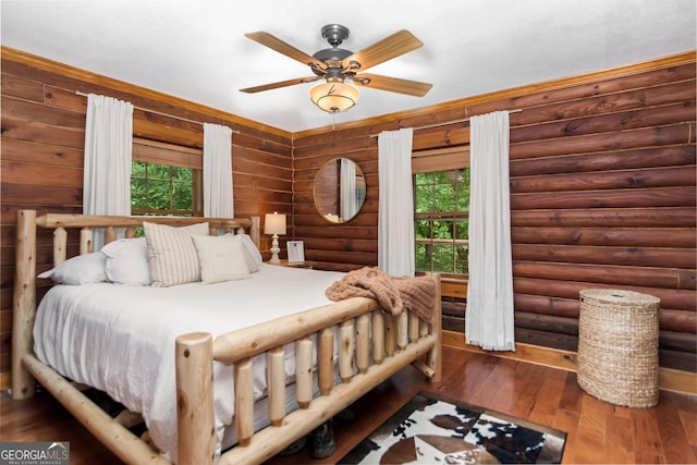 bedroom featuring rustic walls, hardwood / wood-style floors, a ceiling fan, and multiple windows