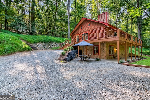 view of front of home with a chimney, stairs, log siding, a patio area, and stone siding